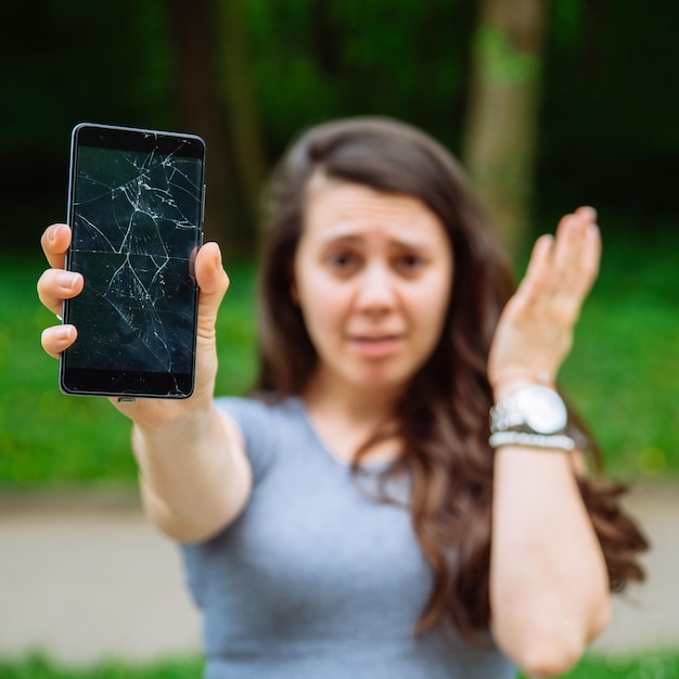 Młoda smutna dorosła kobieta pokazująca pęknięty telefon