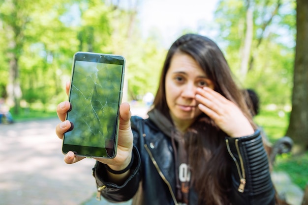 Młoda smutna dorosła kobieta pokazująca pęknięty telefon