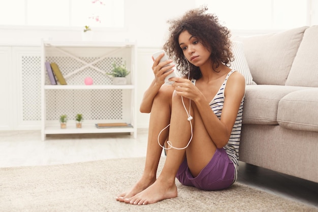 Młoda smutna kobieta zamyślona słuchania muzyki w słuchawkach, siedząc na podłodze w domu, kopia przestrzeń. Depresja, koncepcja samotności