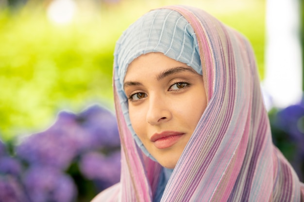 Młoda Spokojna Kobieta W Tradycyjnym Hidżabie Patrzy Na Ciebie, Spędzając Czas W środowisku Miejskim