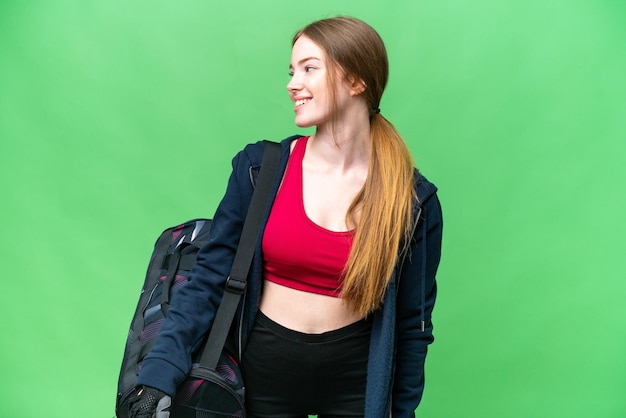 Młoda sportowa kobieta z sportową torbą nad odosobnionym tłem chrominancji, patrząc z boku