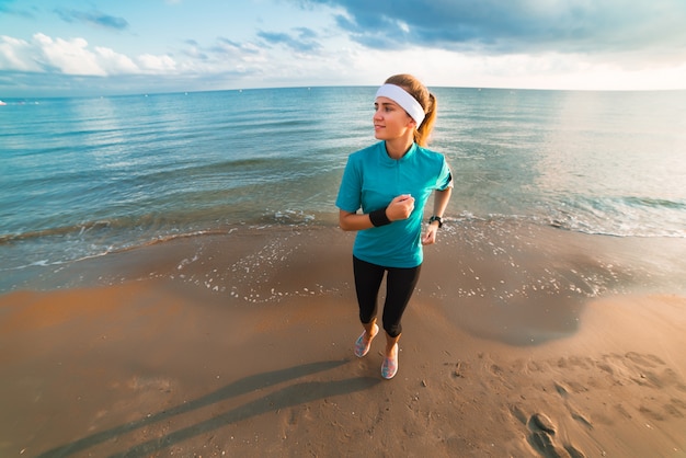 Młoda sporty dziewczyna biega na plaży przy wschodem słońca w ranku