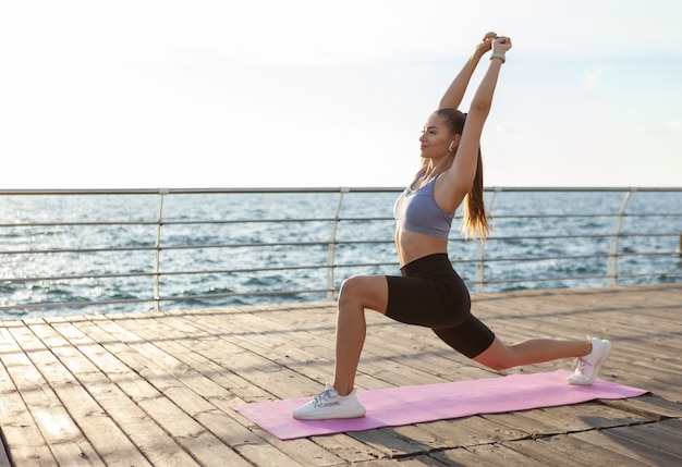 Młoda sprawna kobieta w stroju sportowym ćwiczy pozę ćwiczeń jogi asan o wschodzie słońca na plaży