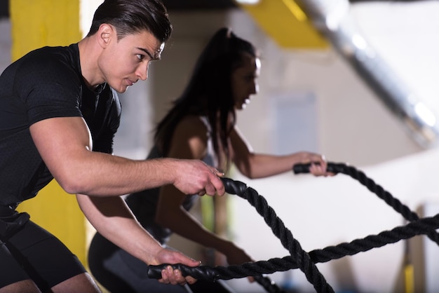 młoda sprawna para sportowa ćwicząca w treningu funkcjonalnym siłownia wykonująca liny bojowe krzyżowe ćwiczenia fitness