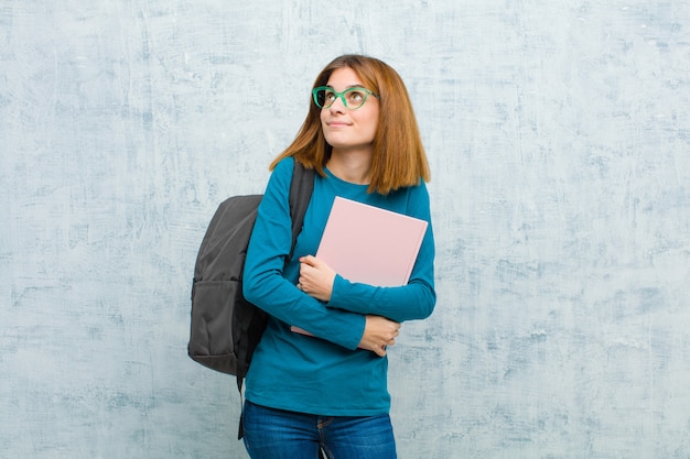 Młoda studencka kobieta czuje się szczęśliwy, dumny i pełen nadziei, zastanawiający się lub myśleć, patrzejący do kopii przestrzeni z krzyżującym ręki tłem