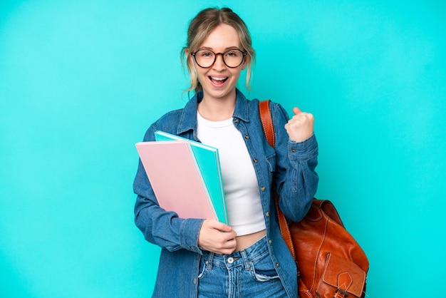 Zdjęcie młoda studencka kobieta odizolowana na niebieskim tle świętuje zwycięstwo w pozycji zwycięzcy