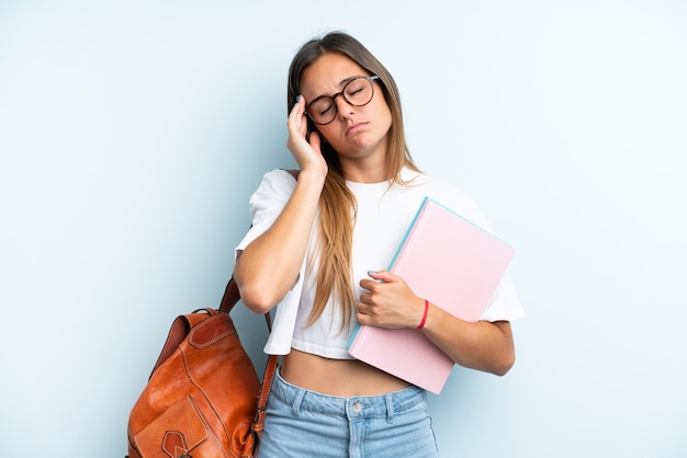 Młoda studencka kobieta odizolowywająca na błękitnym tle z bólem głowy