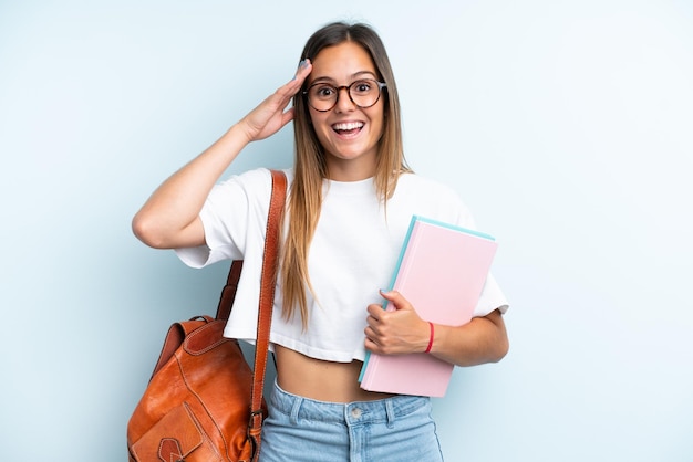 Młoda studencka kobieta odizolowywająca na błękitnym tle z niespodzianką wyrażeniem