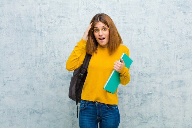 Młoda Studencka Kobieta Patrzeje Szczęśliwą, Zdziwioną I Zdziwioną, Uśmiechając Się I Zdając Sobie Sprawę Z Niesamowitych I Niewiarygodnych Dobrych Wieści Na Tle ściany Grunge