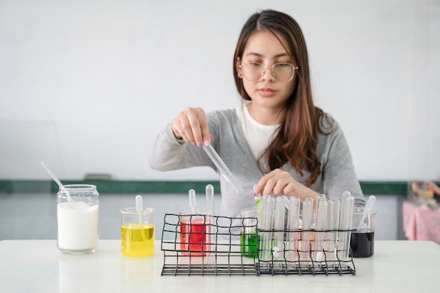 Młoda studentka azjatycka kobieta analizująca i mieszająca płyn w probówce, kolorowa zlewka w laboratorium eksperymentalnym w klasie nauk ścisłych