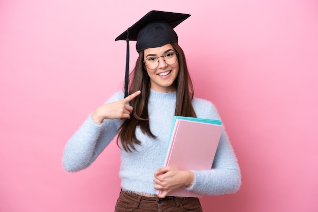 Młoda studentka brazylijska kobieta w kapeluszu z podziałką na białym tle na różowym tle, pokazująca gest kciuka w górę