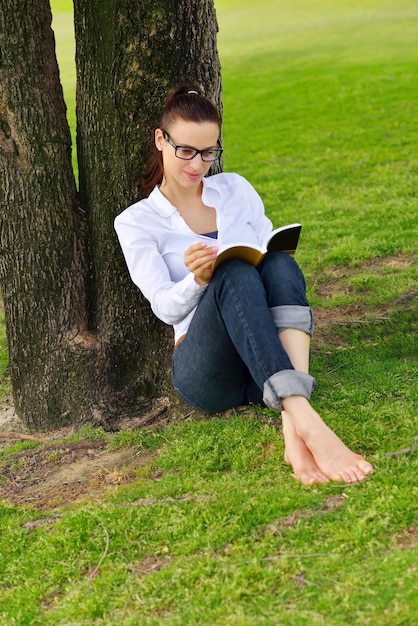 Młoda studentka czytająca książkę i studiująca w parku
