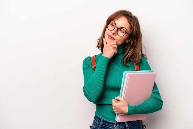 Młoda studentka kaukaska kobieta na białym tle patrząca w bok z wątpliwym i sceptycznym wyrazem twarzy