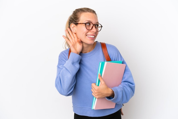 Młoda studentka kaukaska kobieta na białym tle, słuchając czegoś, kładąc rękę na uchu