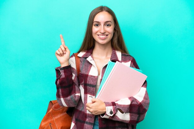 Młoda studentka kaukaska kobieta odizolowana na niebieskim tle, pokazująca i podnosząca palec na znak najlepszych