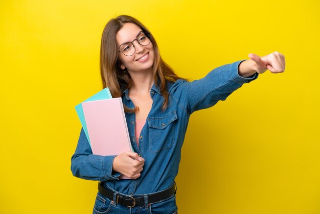 Młoda studentka kaukaska kobieta odizolowana na żółtym tle dająca gest kciuka w górę