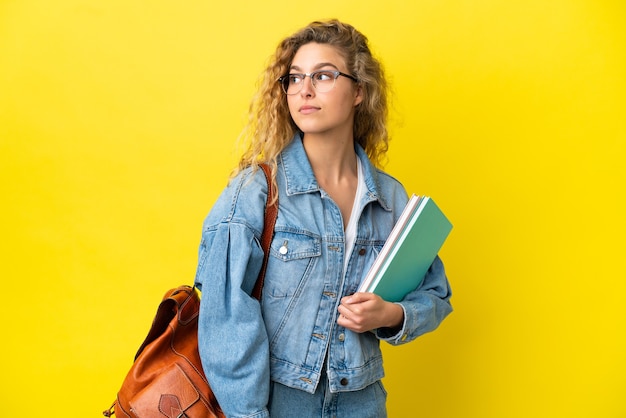 Młoda studentka kaukaska kobieta odizolowana na żółtym tle, patrząc w bok