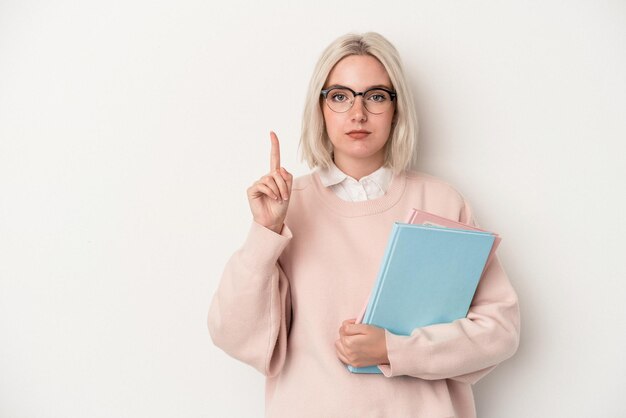 Młoda studentka kaukaska kobieta trzyma książki na białym tle pokazujące numer jeden palcem