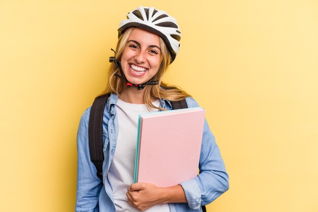 Młoda studentka kaukaski kobieta nosi kask rowerowy na białym tle na żółtym tle szczęśliwa, uśmiechnięta i wesoła.