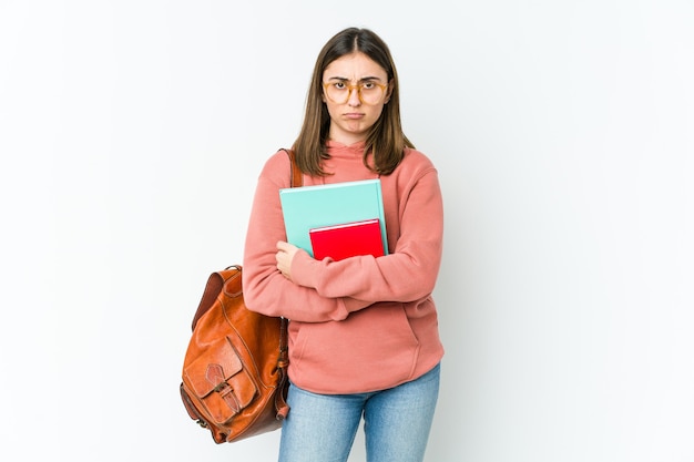 Młoda studentka kobieta na białej ścianie marszczy brwi z niezadowoleniem, trzyma założone ręce