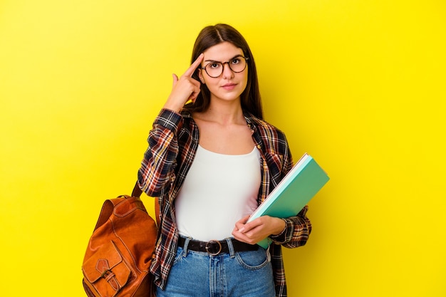 Młoda studentka kobieta na białym tle na żółtej ścianie wskazując świątynię palcem, myśląc, koncentruje się na zadaniu.