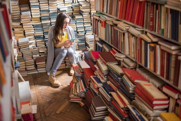 Młoda studentka kobieta siedzi na stosie książek w starej bibliotece