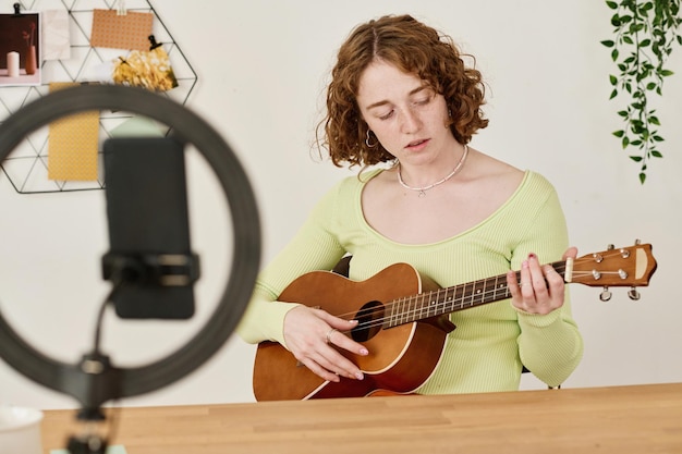 Młoda studentka lub nauczycielka gry na gitarze siedząca przy biurku