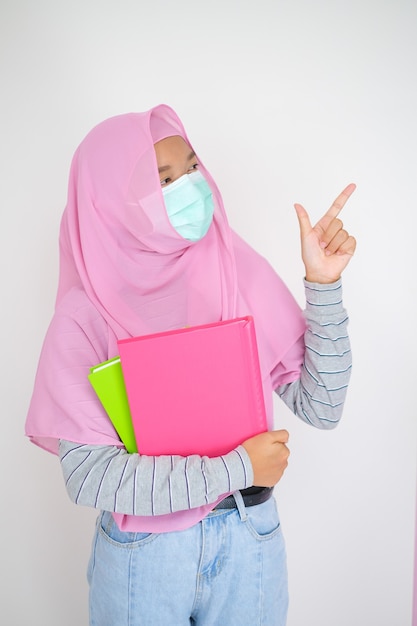 Młoda studentka nosi różowy hidżab i maskę trzyma książki na białym tle