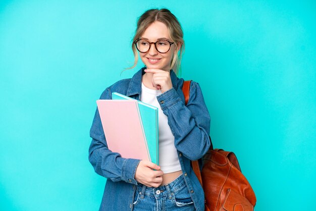 Młoda Studentka Odizolowana Na Niebieskim Tle, Patrząca Z Boku I Uśmiechnięta