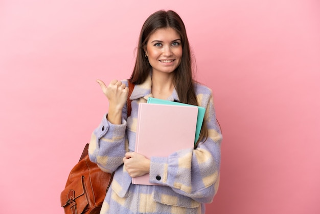 Młoda studentka odizolowana na różowym tle wskazująca na bok, aby zaprezentować produkt