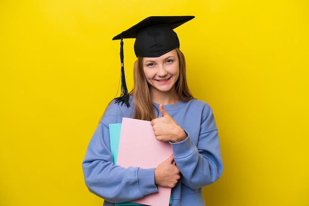 Młoda studentka Rosjanka odizolowana na żółtym tle dająca gest kciuka w górę