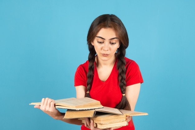 Młoda Studentka W Czerwonej Koszulce Czytając Książkę Na Niebieskiej ścianie.