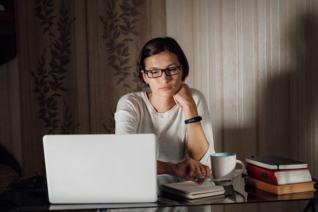 Młoda studentka w okularach za pomocą laptopa komunikuje się w Internecie z nauczycielami