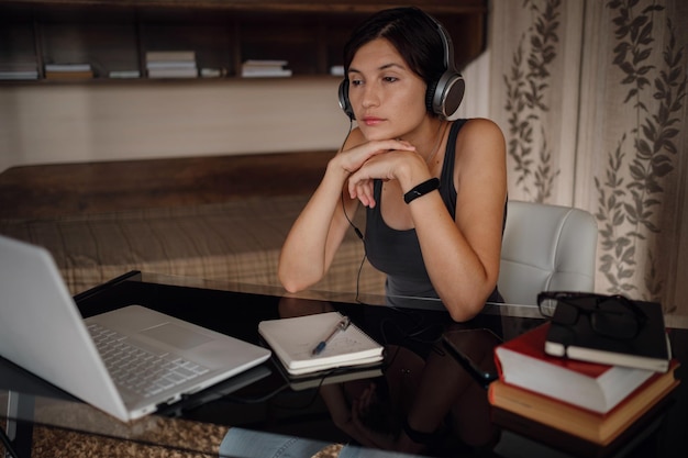 Młoda studentka w słuchawkach za pomocą laptopa komunikuje się w Internecie z nauczycielami