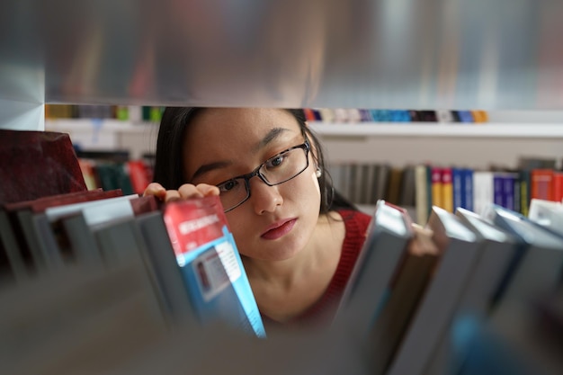 Młoda studentka wybiera książkę z półki w bibliotece uniwersyteckiej do badań edukacyjnych