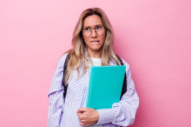 Młoda studentka z Australii na białym tle na różowym tle zdezorientowana, czuje się niepewna i niepewna.