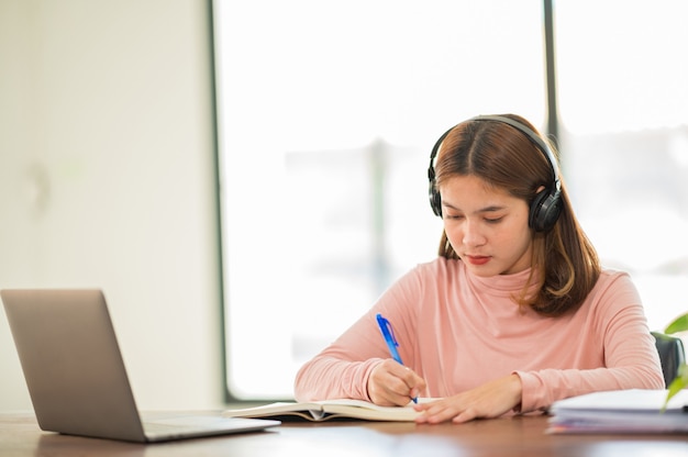 Młoda studentka z Azji w słuchawkach, aby uczyć się online w domu, w czasie epidemii wirusa i nie uczęszczała na uniwersytet.