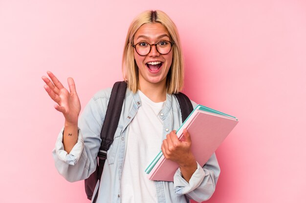 Młoda studentka z Wenezueli na białym tle na różowym tle otrzymująca miłą niespodziankę, podekscytowany i podnoszący ręce.