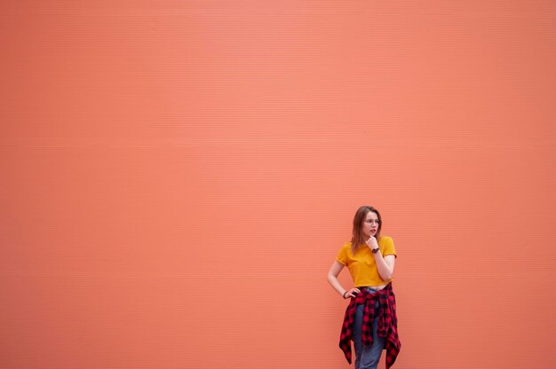 Młoda stylowa dziewczyna stoi na koralowej ścianie i patrzy w kamerę