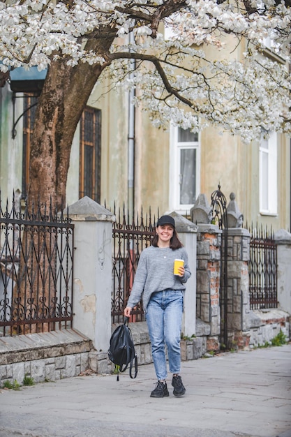 Młoda stylowa kobieta spacerująca ulicą z filiżanką kawy