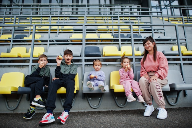 Młoda stylowa matka z czwórką dzieci siedzących na krzesłach na stadionie. Rodzina spędza wolny czas na świeżym powietrzu.
