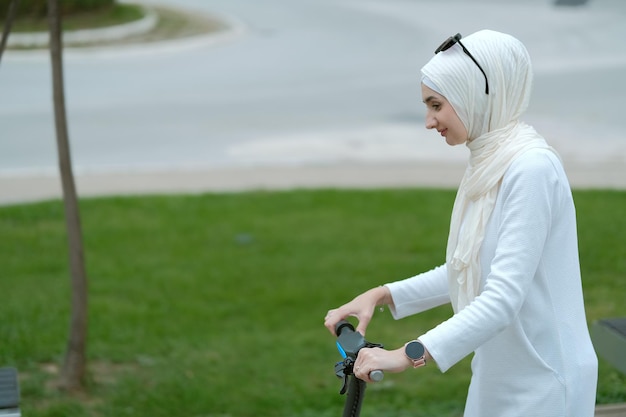 Młoda stylowa muzułmanka w modnym hidżabie jeździ na skuterze elektrycznym po mieście