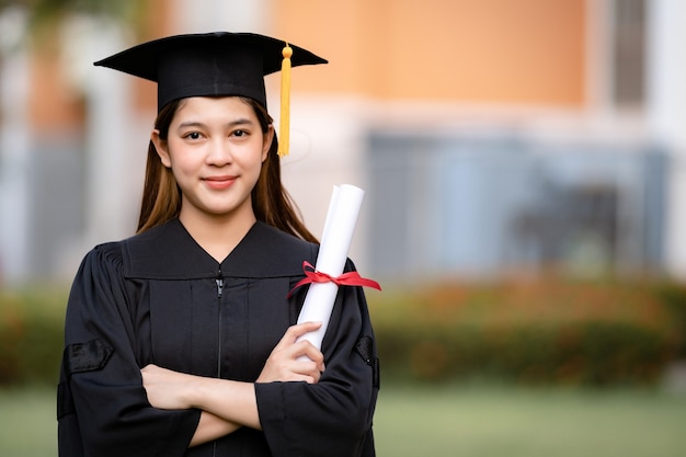 Młoda szczęśliwa absolwentka uniwersytetu Azjatycka kobieta w sukni ukończenia szkoły i tablicy z zaprawą murarską posiada dyplom ukończenia studiów świętuje osiągnięcie edukacji na terenie kampusu uniwersyteckiego. Edukacja pień fotografia