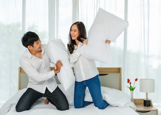 Młoda szczęśliwa atrakcyjna azjatycka para drażni się z walką na poduszki na łóżku.