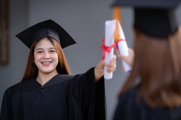 Młoda szczęśliwa azjatycka absolwentka uniwersytetu w sukni ukończenia szkoły i tablicy z zaprawą murarską posiada dyplom świętuje osiągnięcie edukacji w kampusie uniwersyteckim. Edukacja pień fotografia