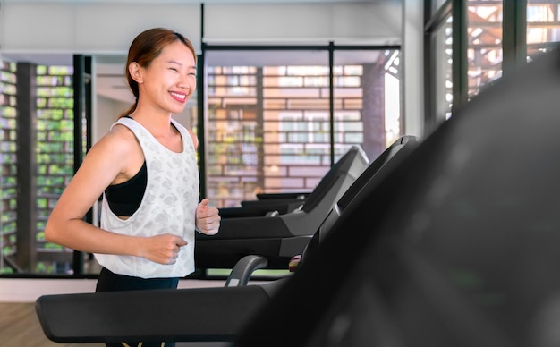 Młoda szczęśliwa azjatycka kobieta sportowiec biega na bieżni w sali gimnastycznej fitness dla zdrowia