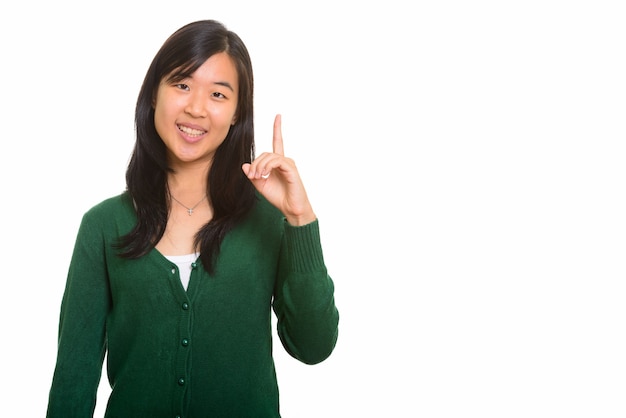 Młoda szczęśliwa Azjatycka kobieta wskazuje palec w górę na białym tle
