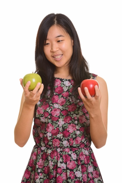 Młoda szczęśliwa azjatycka kobieta wybiera między zielonym i czerwonym jabłkiem na białym tle