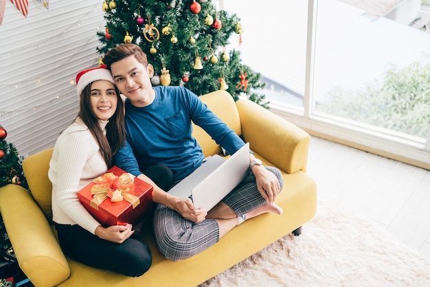 Młoda szczęśliwa azjatycka para siedzi razem podczas rozmowy wideo na laptopie z przyjaciółmi lub rodzicami dzięki za prezent otrzymany podczas świąt Bożego Narodzenia Świętuj koncepcję Boxing Day