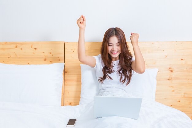 Młoda szczęśliwa azjatykcia kobieta pracuje na jej komputerze w łóżku